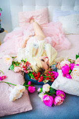 A pretty blond woman in a pink dress with a wreath on her head lying on the bed