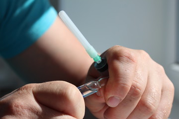 A doctor hand open ampoule and hold with a syringe in his hand
