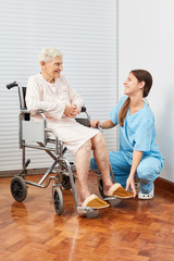 Frau hilft Seniorin beim Anziehen von Hausschuhen