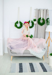 A charming girl in a pink dress, holding green leaves in her hand, sitting on the sofa