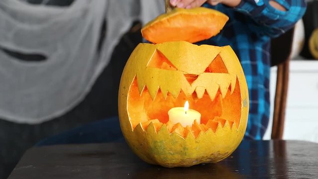 Young boy cutting scary face in pumpkin for Halloween celebration. Closeup view of freshly cutted evil face and burning candle inside of vegetable ready for party. 