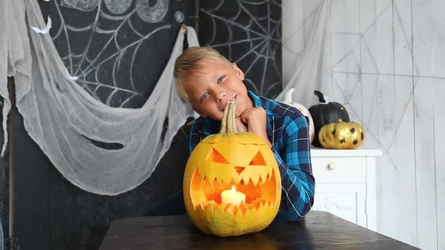 Portrait of cute smiling kid with orange pumpkin at Halloween celebration. Boy posing for photo happily, looks at camera. Real time full hd video footage.