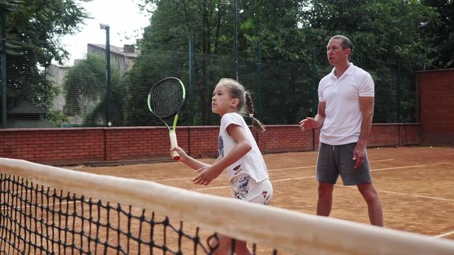 Coacher teaching young girl to playing tennis.