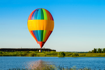 Bright colorful hot air balloon flying over lake in the clear bl