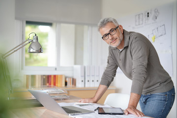 Architect in office sitting on desk looking at camera