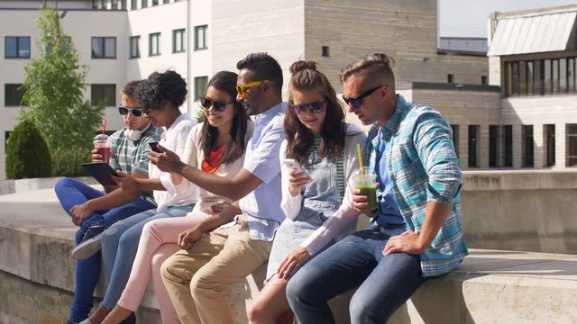 technology, friendship and international concept - group of students or friends with drinks, smartphones and tablet pc in city