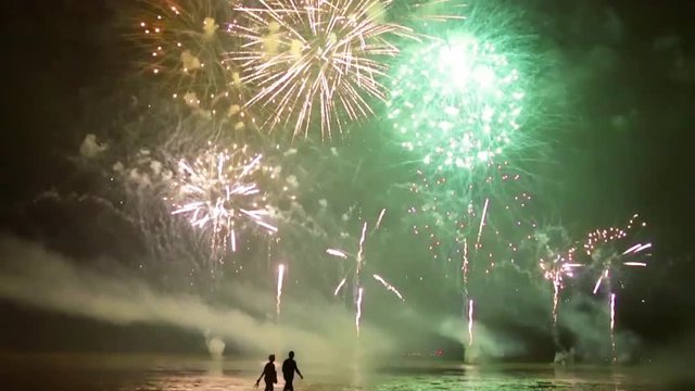 couple of walkers walking on the beach during a firework over the sea. With real sound.