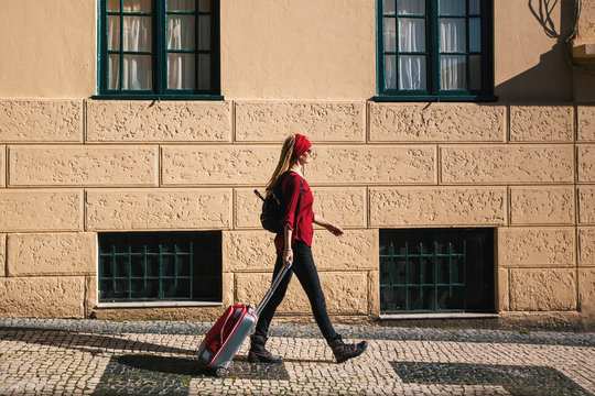 The girl is on the pavement with a red suitcase.