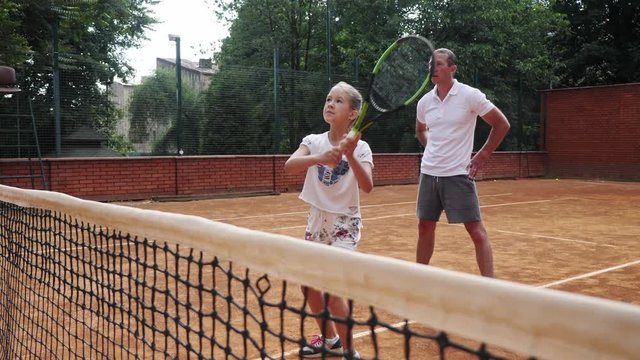 Coacher teaching young girl to playing tennis.