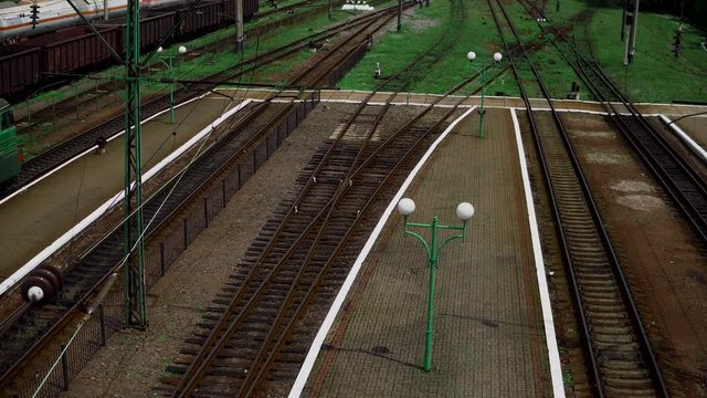 train tracks recede into the distance, amid the remains of the railway platform, a freight train with empty wagons and cisternae, locomotive , some building