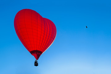 Bright red hot air balloon in the shape of heart against blue sk © smspsy