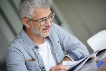 Middle-aged guy with trendy eyeglasses reading magazine