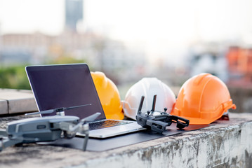 Drone, laptop computer and protective helmet at construction site. Using unmanned aerial vehicle (UAV) for land and building site survey in civil engineering project.