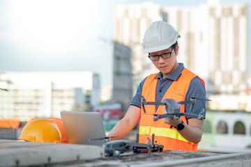 Young Asian man working with drone laptop and smartphone at construction site. Using unmanned...