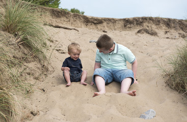 Eleven year old boy playing in the sand with two year old baby brother