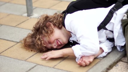 A happy schoolboy is having fun and fooling around. The boy fell on the asphalt and knocks his fist on the paving stone. All fools day, joke, laugh loudly, back to school, farewell school.