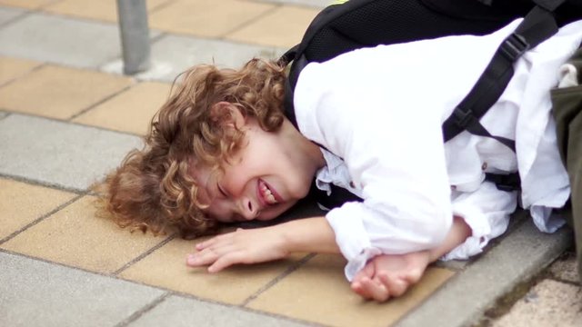 A happy schoolboy is having fun and fooling around. The boy fell on the asphalt and knocks his fist on the paving stone. All fools day, joke, laugh loudly, back to school, farewell school.