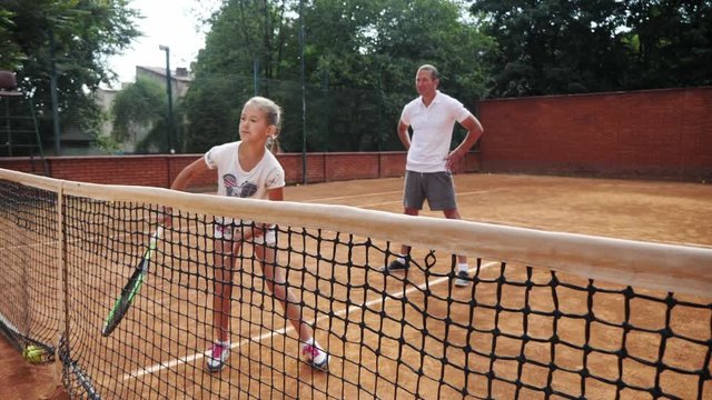 Coacher teaching young girl to playing tennis.