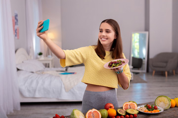 Health in plate. Jolly teen girl using phone and holding plate