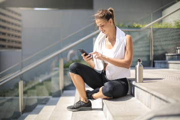 Sportive girl taking a break, sitting down on stairs and checking her phone