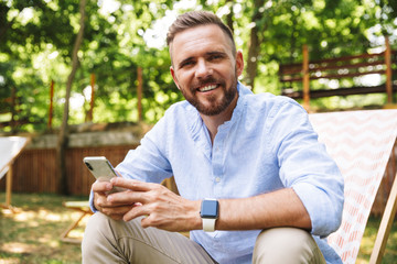 Happy young bearded man outdoors using mobile phone.