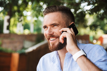 Handsome happy young bearded man talking by mobile phone.