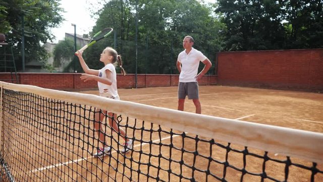 Coacher teaching young girl to playing tennis.