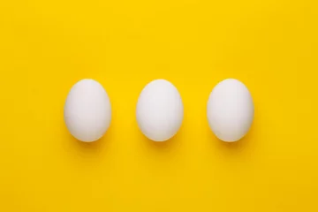 Rolgordijnen Three white eggs on a yellow background. Top view © virtustudio