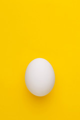 Single white chicken egg on a yellow background. Top view. Copy space