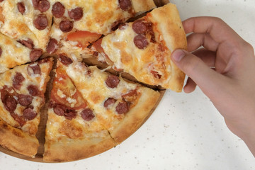 A boy hand taking pizza slice from wooden plate, close up.