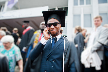 African american happy man at graduation. Graduated student speaking phone at crowd of people.