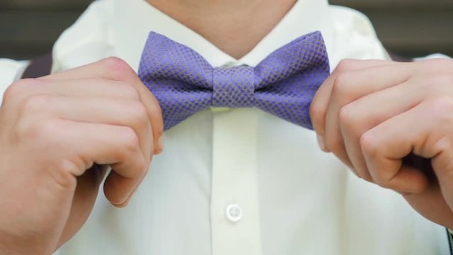 The man straightens his bow tie. Male hands check correct and adjust casual blue bow tie handmade from printed fabrics. Man in a white shirt and suspenders puts on a bow tie.