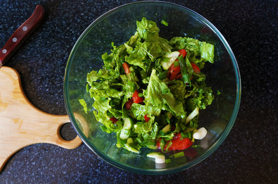 Salad with tomatoes, cucumbers, lettuce and green onions. Dark stone background. View from above.