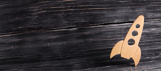 Wooden space rocket in retro style is on a dark wooden background. The space industry, the development of technology and the conquest of space. Creative thinking and business concept. banner