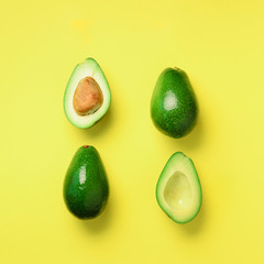 Organic avocado with seed, avocado halves and whole fruits on yellow background. Top view. Square crop. Pop art design, creative summer food concept. Green avocadoes pattern in minimal flat lay style.