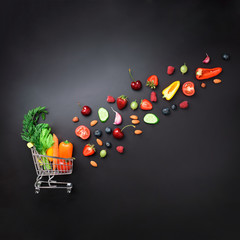 Shopping trolley filled with fresh organic vegetables, fruits and berries on black chalkboard....