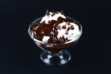 Vanilla ice cream in a white bowl with chocolate on a black background.