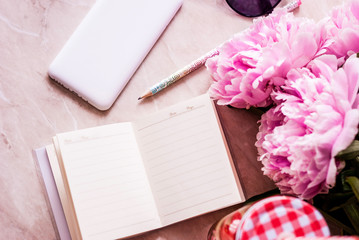 Beauty flat lay with a diary, smartphone, accessories and peonies on a marble background