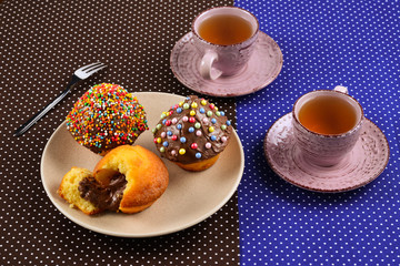 Baking with tea and chocolate on the table.  Two cups of tea with cupcakes and chocolate with a multicolored powder on the table.