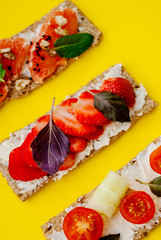 Healthy snack with crispbread, cream cheese, strawberry, grapefruit, tomato and cucumber on a yellow background