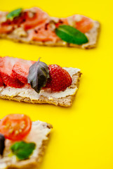 Healthy snack with crispbread, cream cheese, strawberry, grapefruit, tomato and cucumber on a yellow background