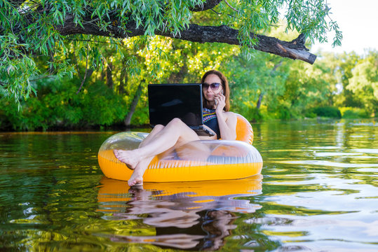 Woman freelancer working on a laptop sitting in an inflatable ring, remote work.