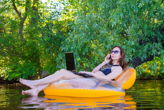 Business woman working on a laptop and talking on smartphone in an inflatable ring in the water, a copy of the free space.