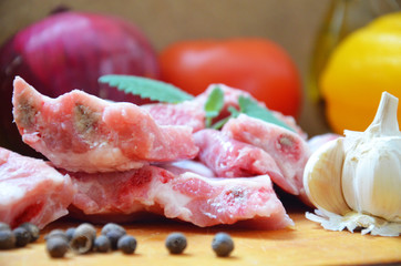 Raw uncooked pork ribs on a paper on dark brown wooden background. Ingredients for meat raw pork ribs sage, thyme, rosemary, pepper, basil, salt.