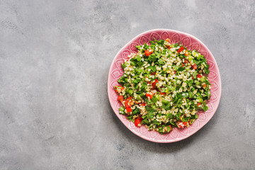 Fototapeta na wymiar Tabbouleh salad, plate, rustic concrete background.Traditional Lebanese dish. Middle Eastern diet food. Top view, copy space.