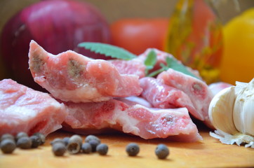 Raw uncooked pork ribs on a paper on dark brown wooden background. Ingredients for meat raw pork ribs sage, thyme, rosemary, pepper, basil, salt.