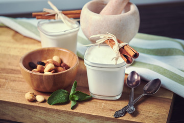 Two glass jars of homemade yogurt and a wooden bowl with nuts on a wooden board with two vintage teaspoons. Pink marble pounder for chopping nuts and cinnamon.