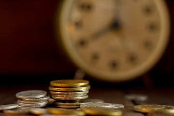 Time is money! Coins in a pile and an clock in the dark background.