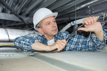 Electrician bending cable in roof space