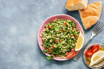 Middle Eastern or Arab food on a blue rustic background , tabbouleh salad and pita bread. Lebanese traditional dish, flat lay, copy space.